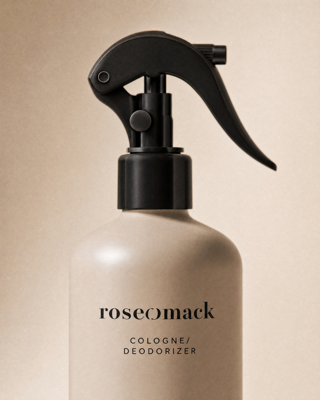 Close view of the black trigger and the roseomack wordmark on the greige Cologne bottle