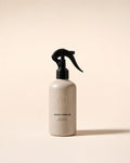 roseomack Cologne, a greige bottle with a black trigger spray, standing alone on a pale sand backdrop