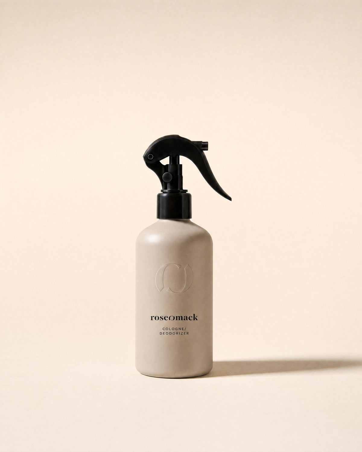 roseomack Cologne, a greige bottle with a black trigger spray, standing alone on a pale sand backdrop