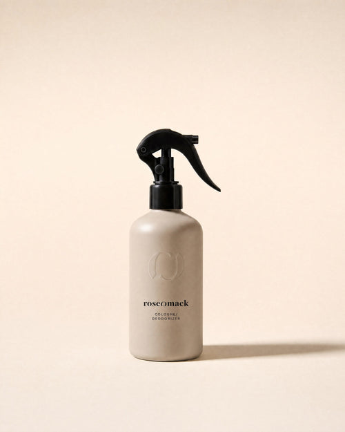 roseomack Cologne, a greige bottle with a black trigger spray, standing alone on a pale sand backdrop