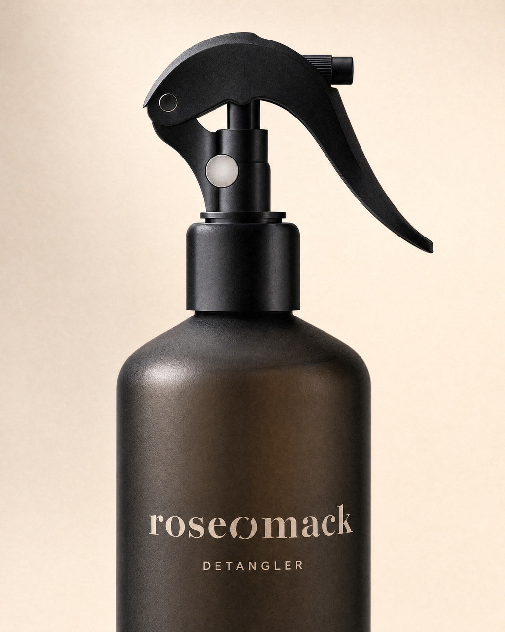 Close view of the black trigger and beige wordmark on the dark brown roseomack Detangler bottle