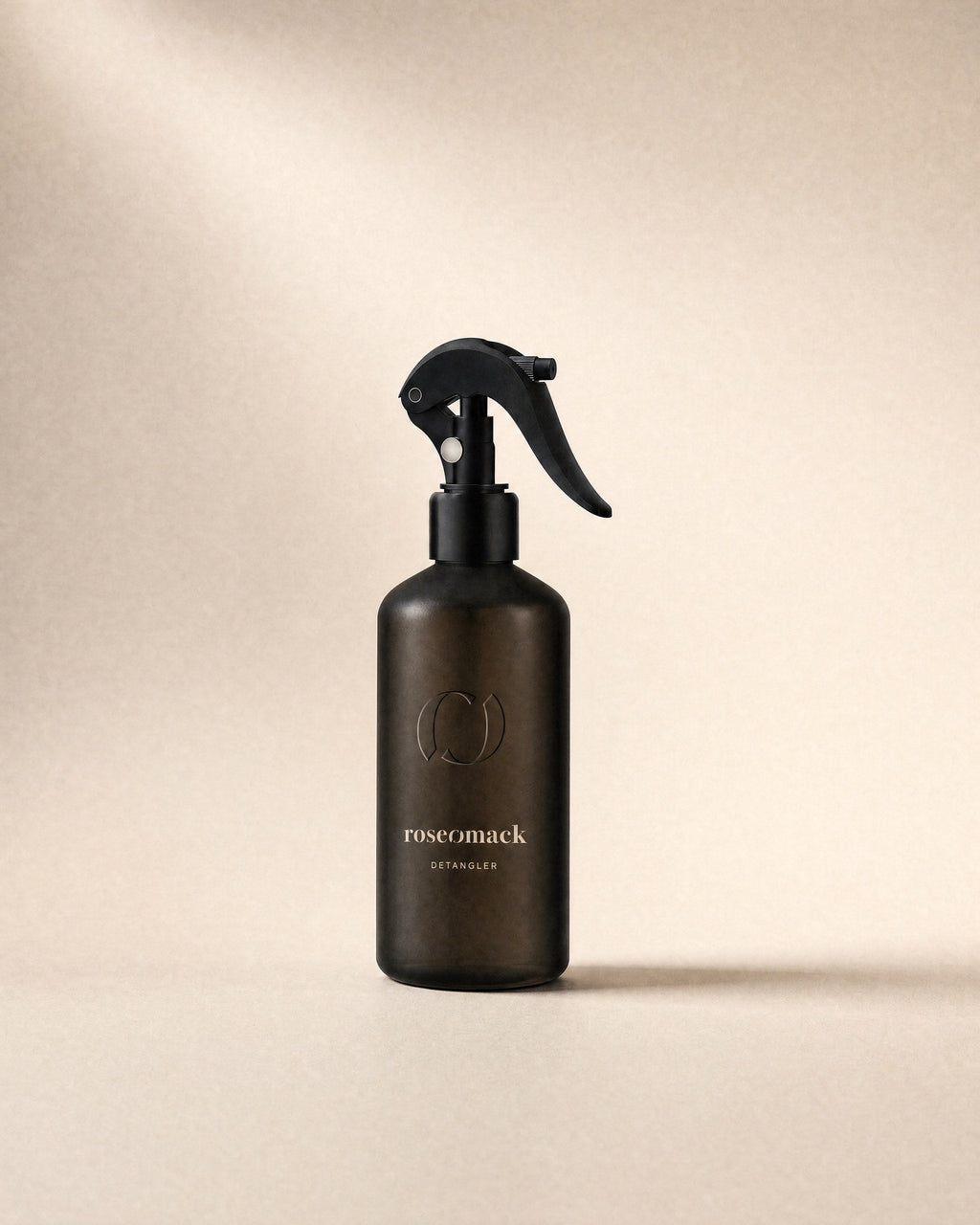 roseomack Detangler, a frosted dark brown bottle with a black trigger spray, on a sand backdrop