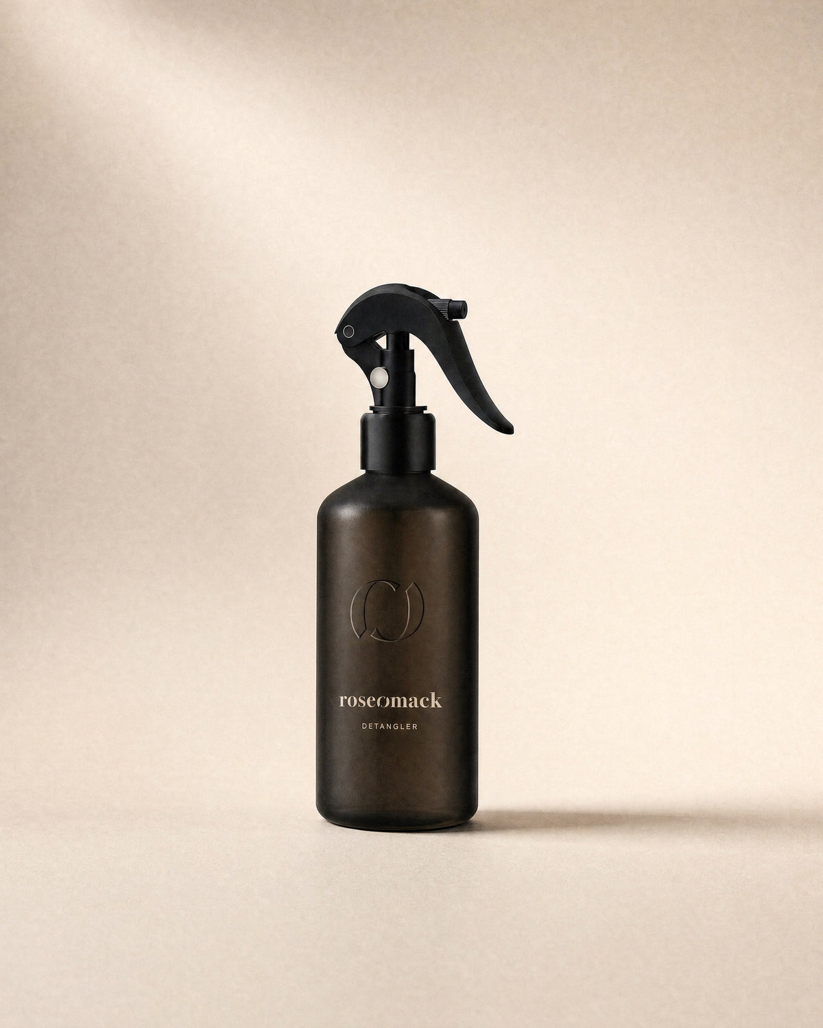 roseomack Detangler, a frosted dark brown bottle with a black trigger spray, on a sand backdrop