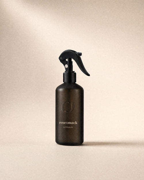 roseomack Detangler, a frosted dark brown bottle with a black trigger spray, on a sand backdrop