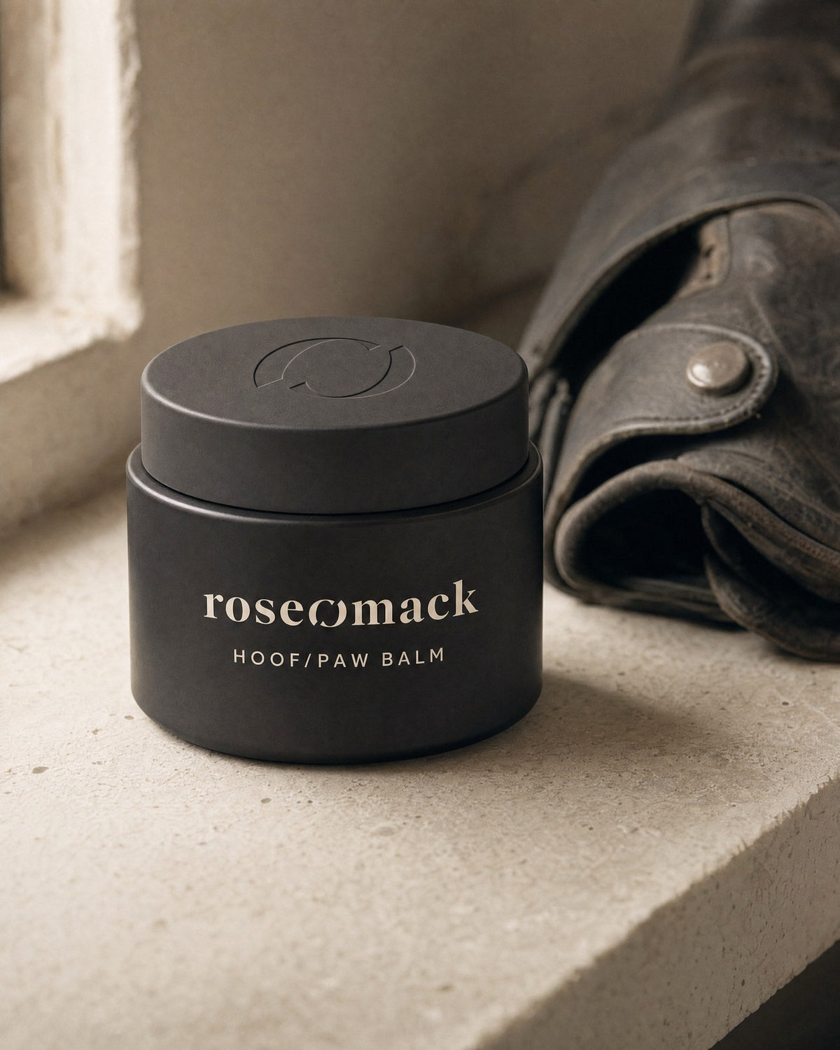 roseomack Hoof & paw balm on a pale stone window ledge beside a piece of worn, folded leather