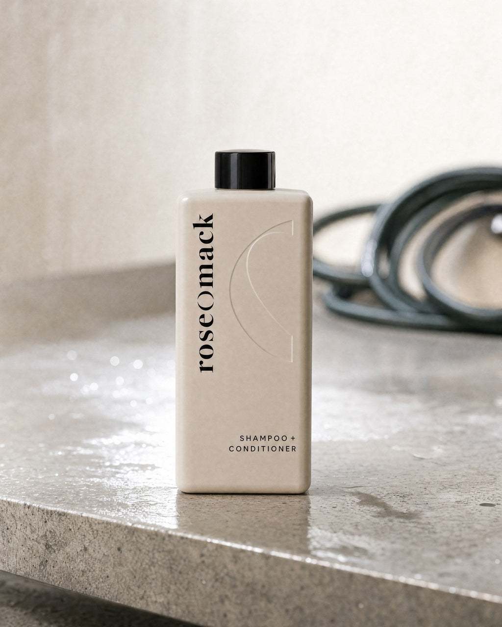 roseomack Shampoo & conditioner on a wet stone ledge in a wash bay, a coiled green hose behind