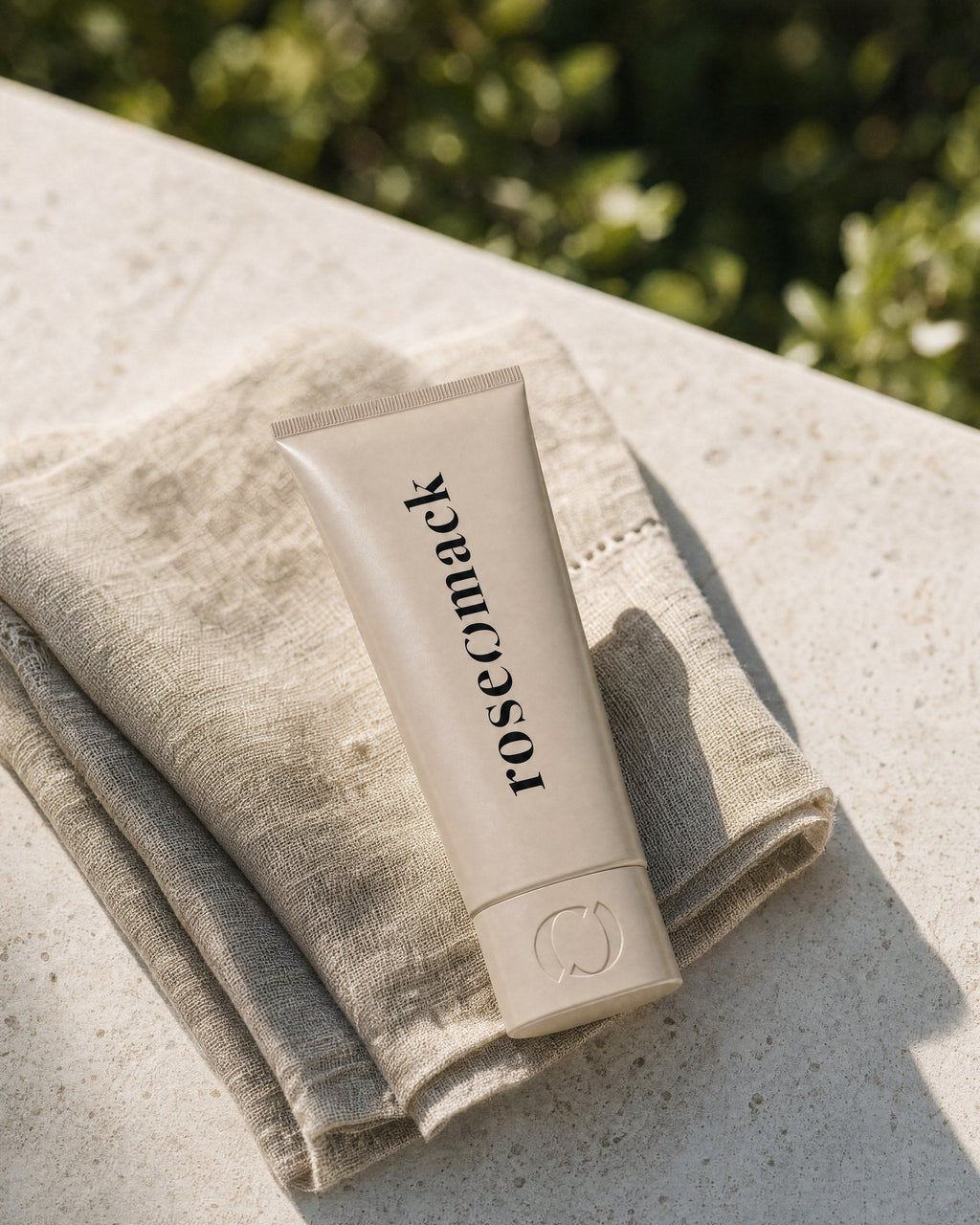 roseomack Sun protection tube on a folded linen cloth on a sunlit stone ledge, green leaves behind