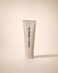 roseomack Sun protection, a slim greige squeeze tube standing on its cap, on a sand backdrop
