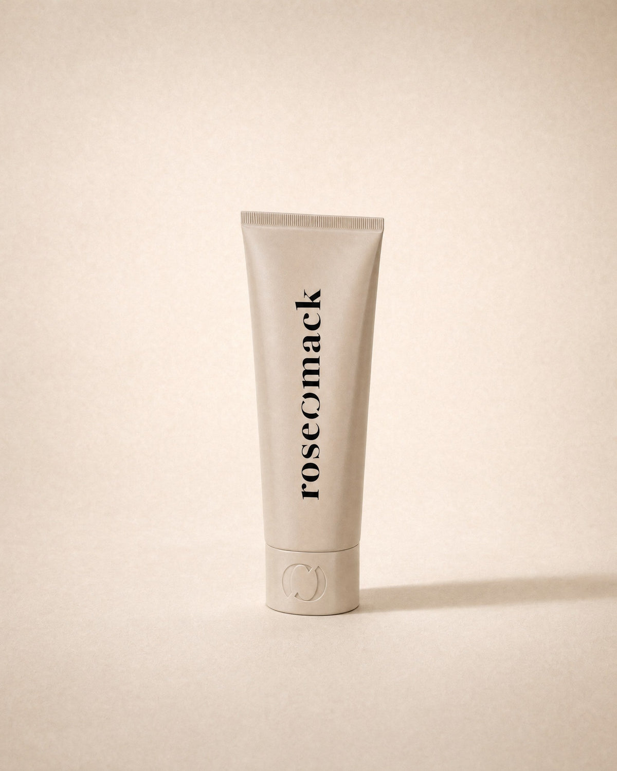 roseomack Sun protection, a slim greige squeeze tube standing on its cap, on a sand backdrop